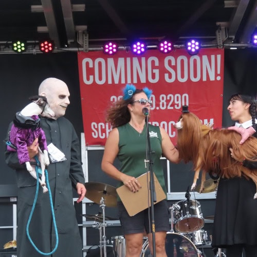 The Adams Family are up on stage; puppy versions of Gomez and Uncle Ibb with their humans dressed as Uncle Fester and Wednesday Adams.