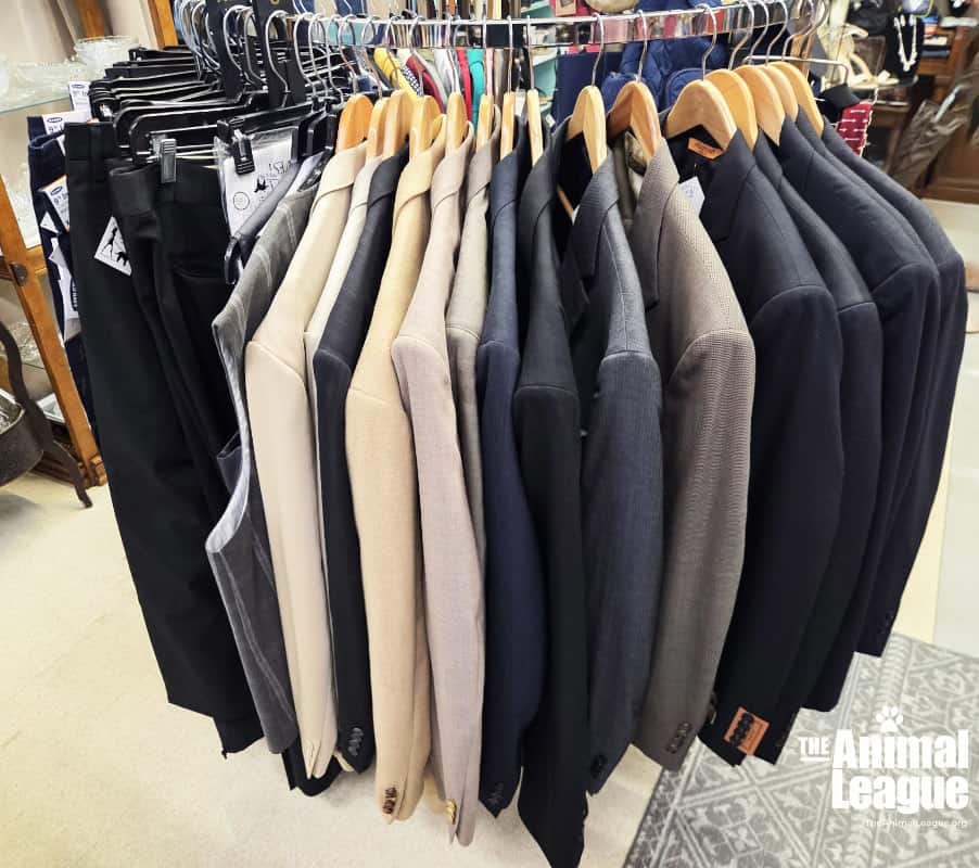 Jackets, vests, and pants in different shades of cream, tan, grey, brown, and black hang from wooden hangers on a round rack.